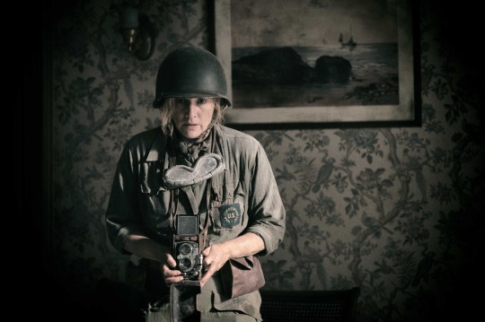 Kate Winslet as Lee Miller in Lee, holding a camera and dressing up in military uniform